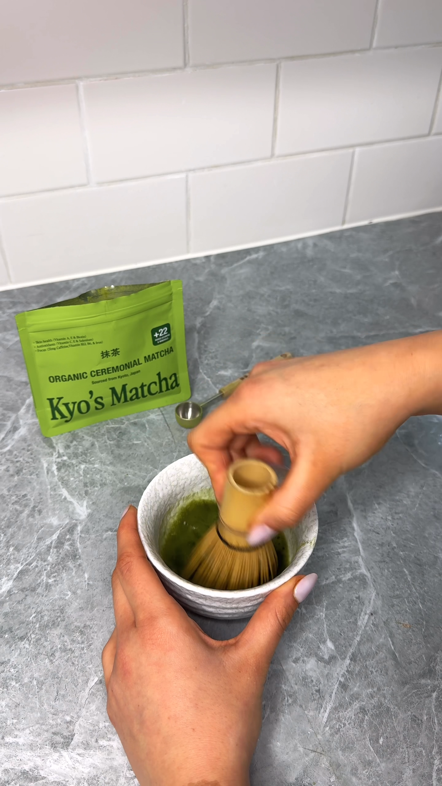 Person making matcha tea with a Kyo's Matcha packet on a gray countertop.